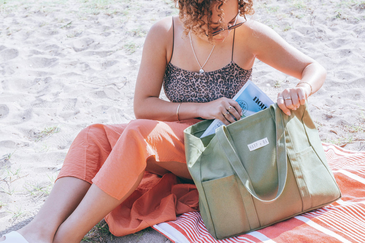 Woman at the beach packing a magazine into the Harp + Ra Origin Tote in Forest Green