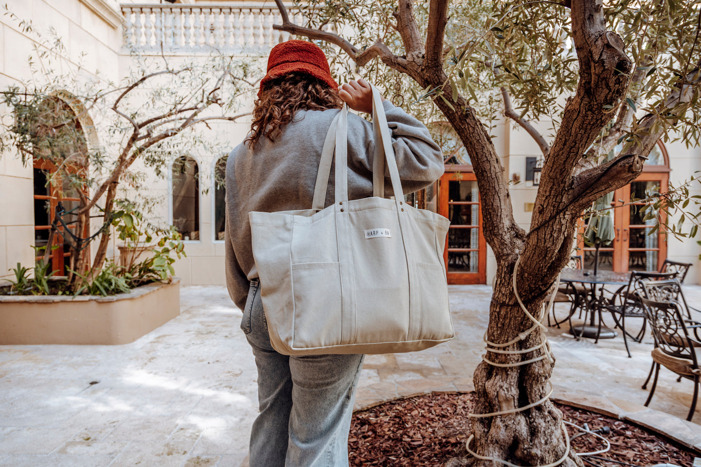 Extra large tote bag is used in a garden area by a girl she is holding the bag over her shoulder with long shoulder straps, bag is full of travel accessories