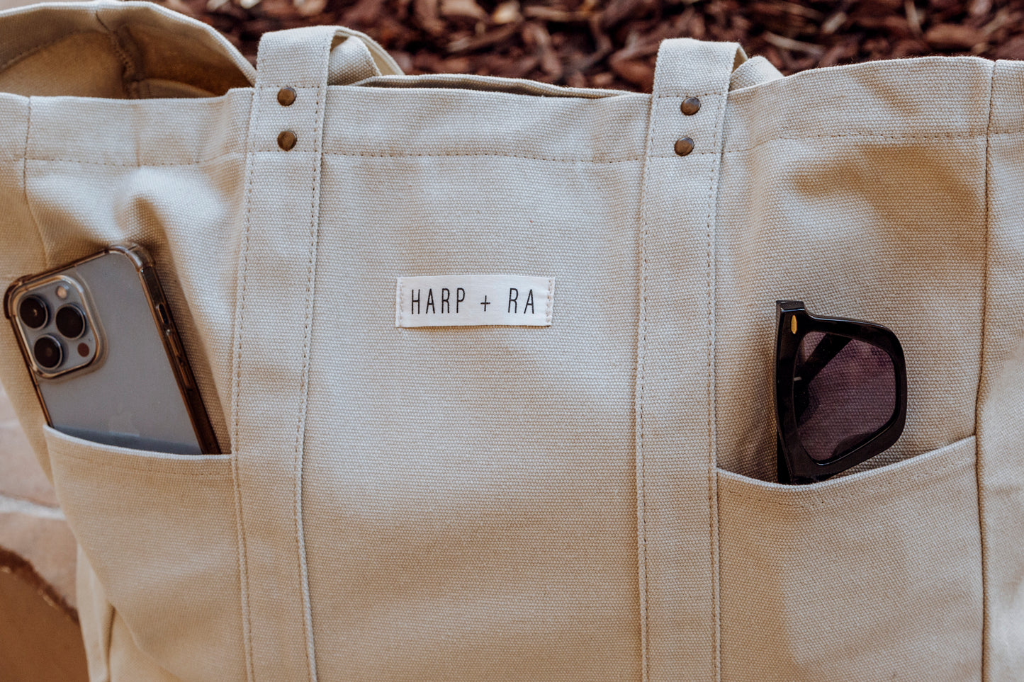 Large canvas beige tote bag showing features of two front pockets measuring 11 inces wide that can fit sunglasses and a large i-phone easily, fabric is soft yet heavy duty and strudy